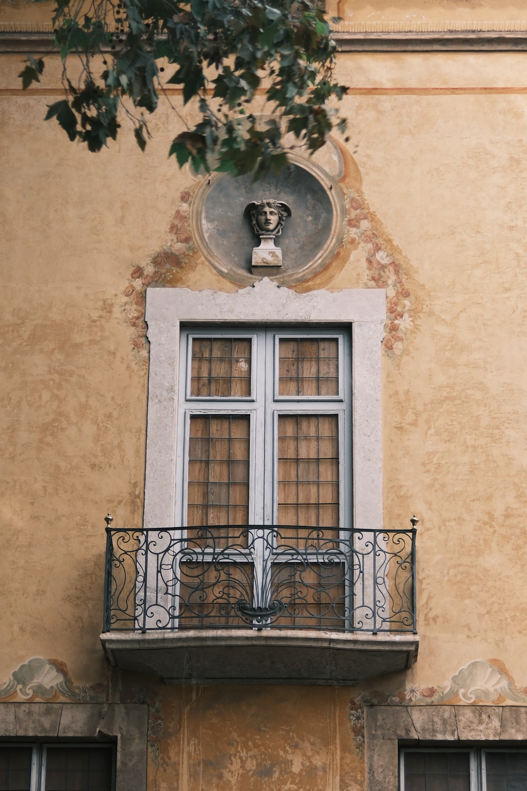 Fachada ocre con un balcón de hierro forjado y una ventana con marco de piedra