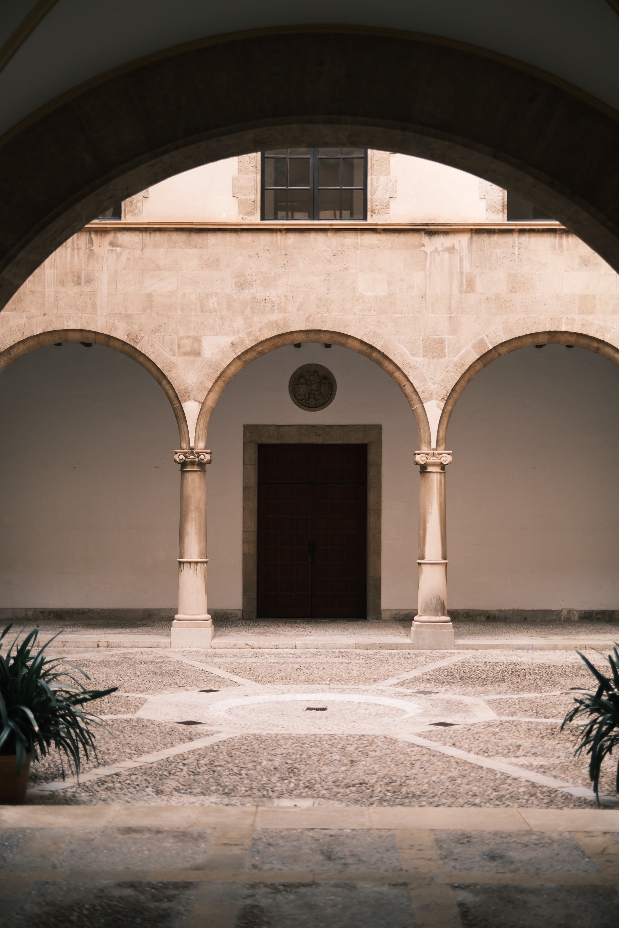 Patio de piedra con arcos y una puerta de madera al fondo, visto desde un arco