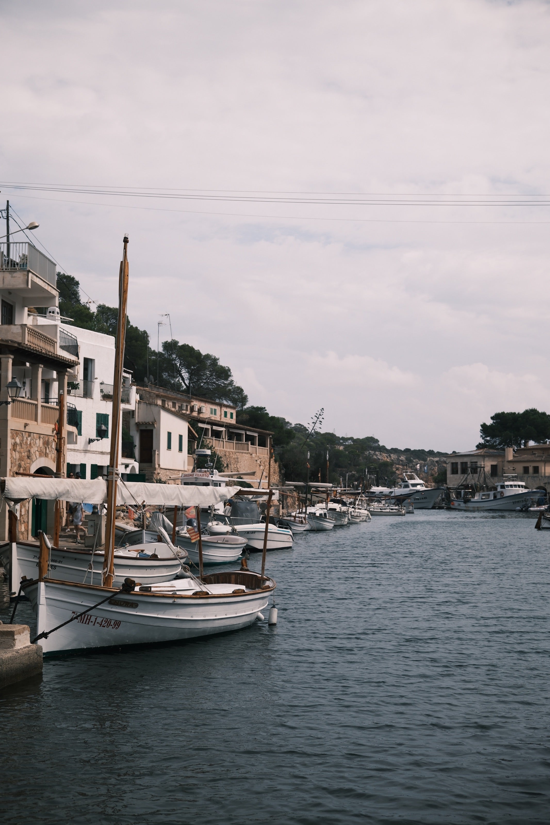 Canal estrecho de aguas oscuras con llaüts amarrados y casas blancas a lo largo de la orilla