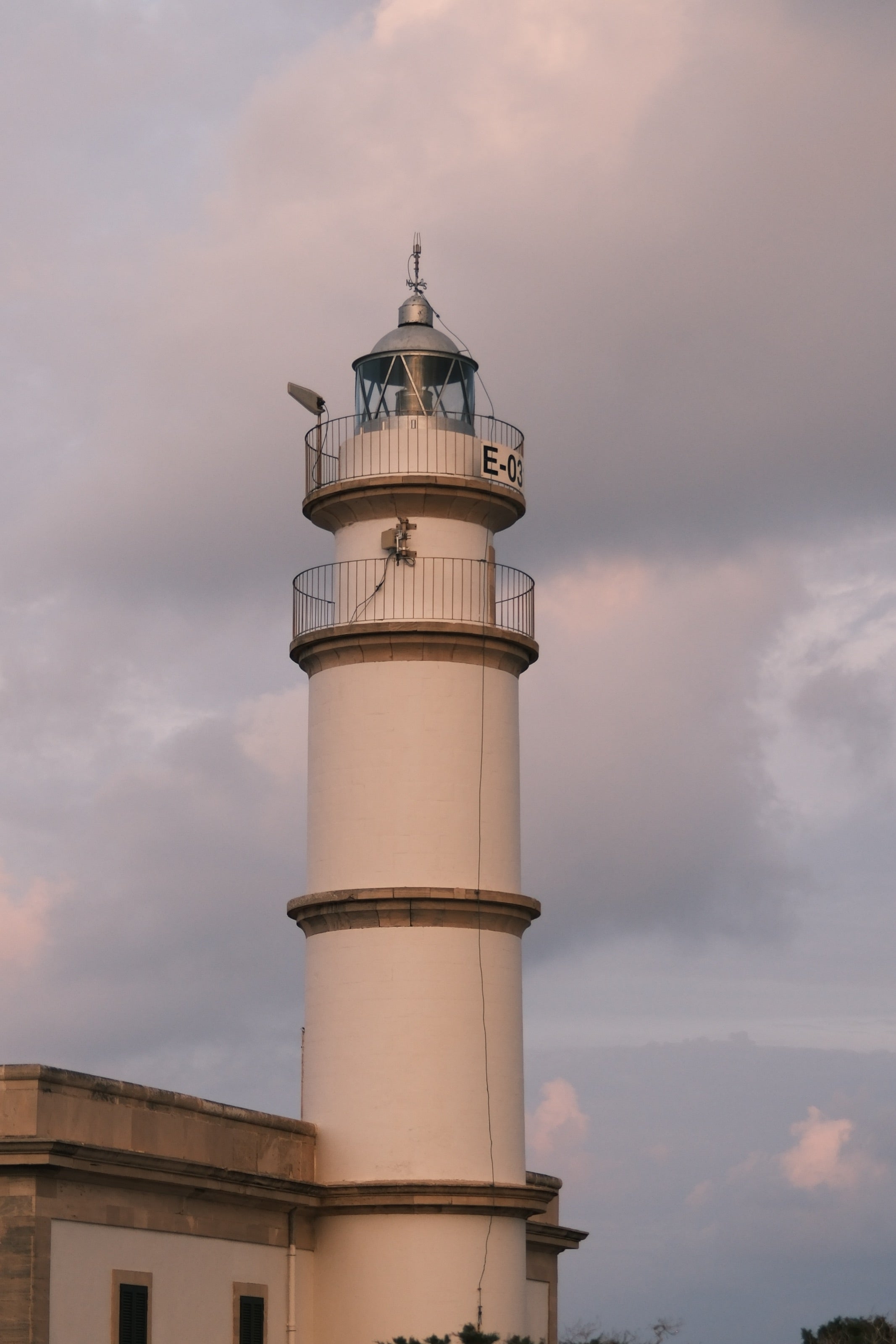 Faro de color crema bajo un cielo de nubes rosadas y luz cálida al final del día